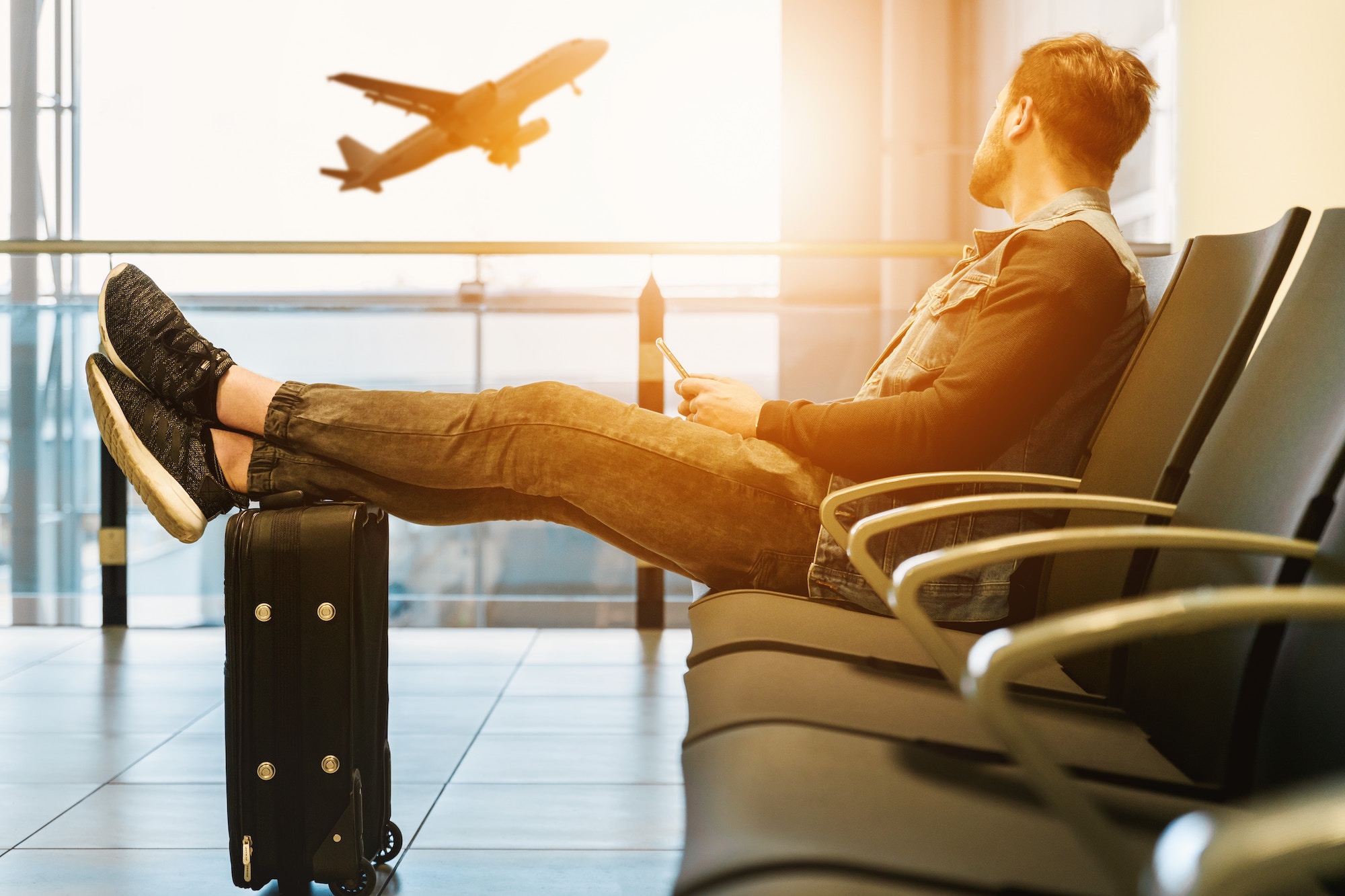 man at airport gate with feet on luggage prepared with travel health